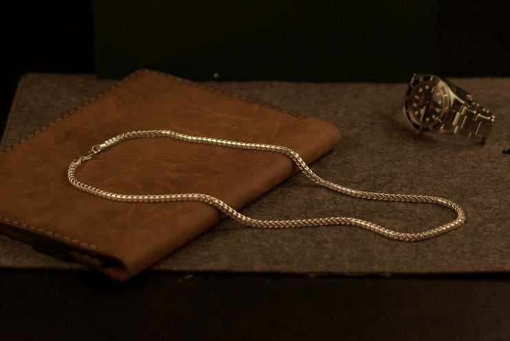 A jeweler crafting a sterling silver chain on a workbench, highlighting meticulous craftsmanship and precision tools.